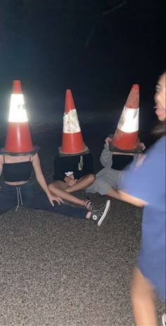 three people sitting on the ground in front of traffic cones