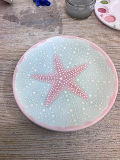 a pink and blue plate with a starfish painted on the side sitting on a wooden table