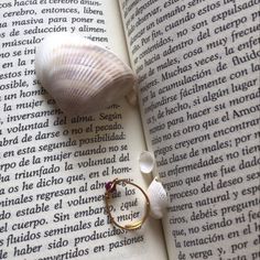 an open book with a ring on top of it next to a seashell and sea shells