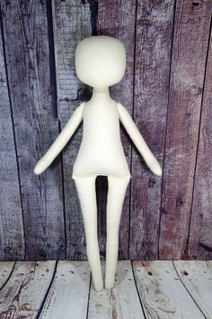 a white doll standing on top of a wooden floor next to a wood plank wall