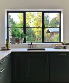 a kitchen with black cabinets and white counter tops is seen through the window, while plants are in pots on the windowsill