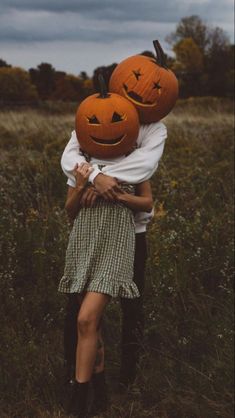 two people are hugging each other with pumpkins on their heads in the middle of a field