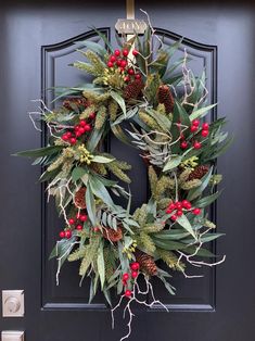 a christmas wreath hanging on the front door with holly and red berries, greenery and pine cones