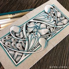 an intricately designed piece of paper on top of a wooden table next to colored pencils