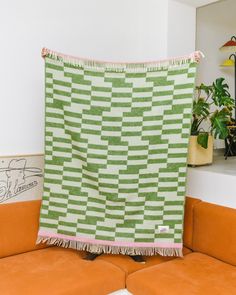 a green and white blanket sitting on top of a couch next to a potted plant