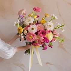 a woman holding a bouquet of flowers in her hands on a marble surface with pink, yellow and white colors