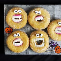 four doughnuts with faces and mouths are on a baking sheet in front of a black background