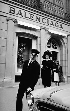 black and white photograph of two women in front of a building with an old car