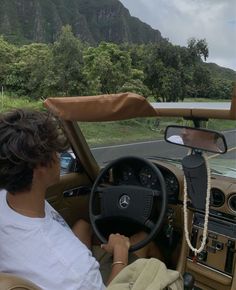 a man sitting in the driver's seat of a car with mountains in the background