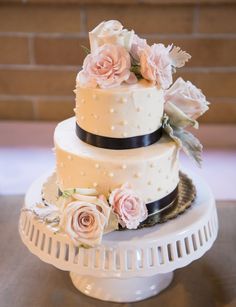 a three tiered wedding cake with pink flowers on the top and black ribbon around it