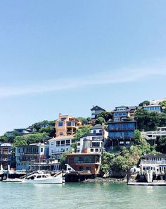 the houses are on top of the hill by the water's edge, with boats in the foreground