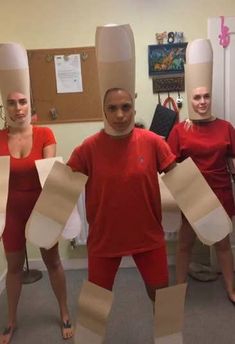 three people in red shirts and white paper hats are holding up large pieces of cardboard