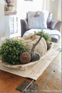 a table topped with pumpkins and greenery on top of a piece of cloth