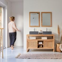 a woman standing in front of a bathroom sink next to a mirror and wooden cabinet