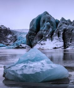 an iceberg floating on top of a lake surrounded by mountains