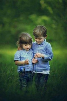 two little boys standing in the grass with their arms around each other and looking at something