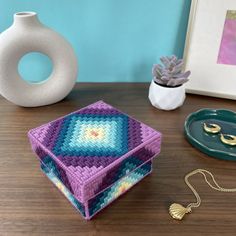 a crocheted box sitting on top of a wooden table next to a vase