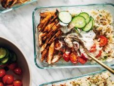 four glass containers filled with food on top of a white marble counter topped with cucumbers, tomatoes and other vegetables