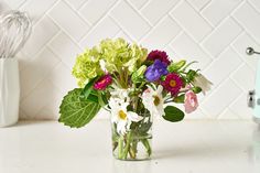 a glass vase filled with colorful flowers on top of a counter next to a mixer