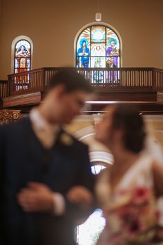 a bride and groom standing in front of a stained glass window