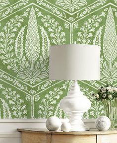 a lamp on a table next to a green wallpaper with white flowers and leaves