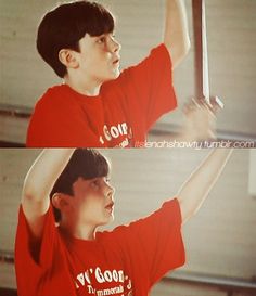 a boy in a red shirt holding up a baseball bat with both hands and the other arm above his head