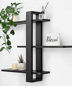 two black shelves with plants on them against a white wall, one shelf has a plant in it and the other is empty