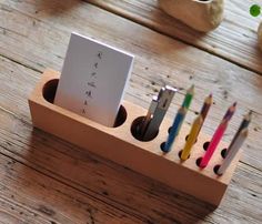 a pen holder with pens and pencils in it on a wooden table next to potted plants