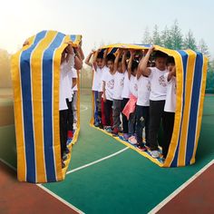 a group of children standing on top of a tennis court holding up a giant mirror