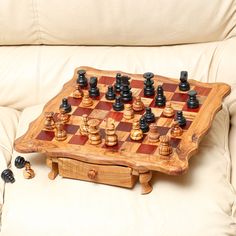 a wooden chess board sitting on top of a couch next to black and white pieces