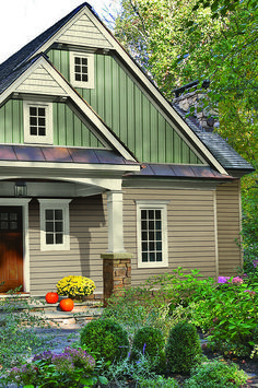 a small gray house with white trim and two large windows on the front door, surrounded by greenery