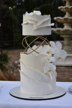 a three tiered wedding cake with white flowers on the top and gold spirals