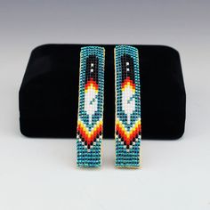 NATIVE AMERICAN NAVAJO BEADED BARRETTES BY MIKE NATHANIEL Navajo artist Mike Nathaniel hand beaded these beautiful barrettes.  Great colors that compliment the design.  Mike uses tiny seed beads to create his jewelry and backs it with soft leather. 1/2” wide x 2  1/2” long Artist card included When trade beads were introduced to Native Americans, they made these colorful glass beads part of their jewelry.  Over the years, glass beads have been used to complement traditional designs and to adorn everything from clothing to ceremonial objects.  Artists from the Navajo Reservation in the Four Corners Area, bead a variety of items, such as bracelets, key rings, barrettes, rattles, earrings, and much more.  With beautiful designs and brilliant colors, Native American beadwork is appreciated by Beaded Hairties, Bead Loom Patterns Native, Beaded Barrettes, Navajo Reservation, Native American Dress, Indian Beadwork, American Dress, Native American Beaded Earrings, Artist Card