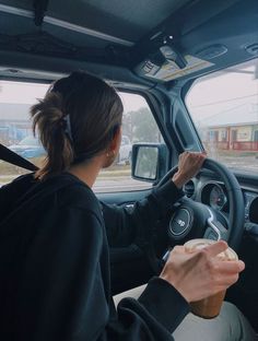 a woman sitting in the driver's seat of a car holding a cup of coffee