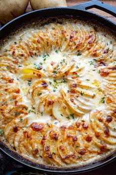 a baked dish with potatoes and cheese in a cast iron skillet on a wooden table