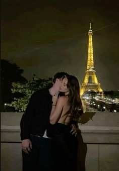 a man and woman kissing in front of the eiffel tower, at night