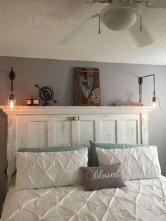 a white bed topped with pillows next to a wall mounted fan and light bulb on top of the headboard