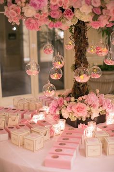 a table topped with lots of pink flowers and boxes under a tree filled with bubbles