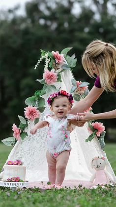 a baby girl standing in front of a teepee with flowers on it