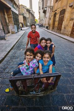 a group of young children riding on the back of a wooden cart down a cobblestone street