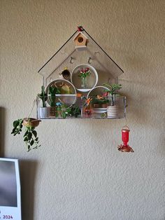 a bird house hanging from the side of a wall with potted plants in it