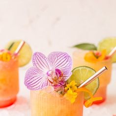 three cocktails with flowers and lime garnishes on the rim, sitting on ice