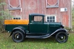 an old green truck parked in front of a red barn