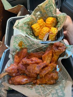 two trays filled with fried chicken and corn on the cob next to each other