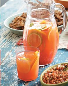 a pitcher and two glasses filled with drinks on top of a blue wooden table next to plates of food