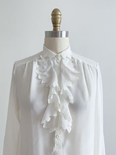 A darling silky white blouse, with jabot style ruffles with embroidered edges. ☛ m e a s u r e m e n t s ☚ Best for: XS-S Bust: 34 Waist: 34 Shoulders: 14 Length: 24 ☛ d e t a i l s ☚ Era: 1980s Material: polyester Condition: excellent ☛ v i s i t   t h e   s h o p ☚ https://etsy.me/2Nd23kg ☛ instagram ┇ poppycockvintage ☛ facebook ┇ poppycockvintage Feminine White Blouse With Ruffles, Formal Collared Ruffle Blouse, Formal Ruffled Collared Blouse, Elegant Collared Blouse With Ruffles, Formal Collared Blouse With Ruffles, Formal Blouse With Ruffles And Ruffled Collar, Feminine Collared Blouse With Ruffles, Spring Vintage White Blouse With Ruffles, Feminine Blouse With Ruffle Hem And Ruffled Collar