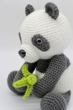 a crocheted panda bear holding a green plant