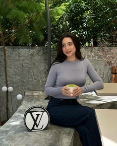 a woman sitting on top of a cement bench holding a green bowl in her hands