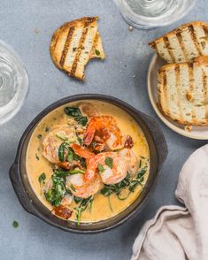 a bowl of soup with shrimp and spinach next to grilled bread on the side