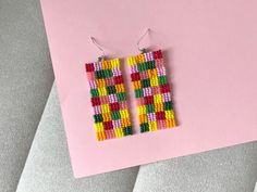 a pair of colorful beaded earrings sitting on top of a pink surface